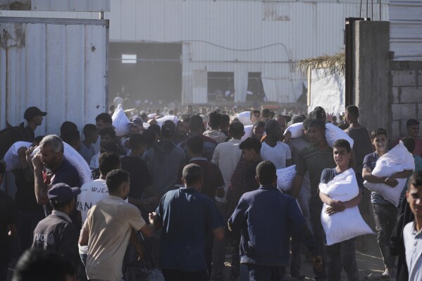 Palestinians carry bags of flour after storming a U.N. World Food Program warehouse in Zawaida, Central Gaza Strip, on Wednesday, May 28, 2025. (AP Photo/Abdel Kareem Hana)